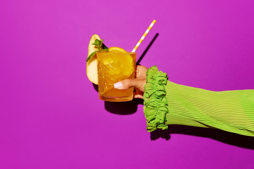 Hand,Holding,Glass,Of,Screwdriver,Cocktail,With,Colorful,Tube,Over